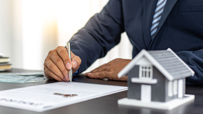 Businessman in suit signing real estate contract with house model on desk