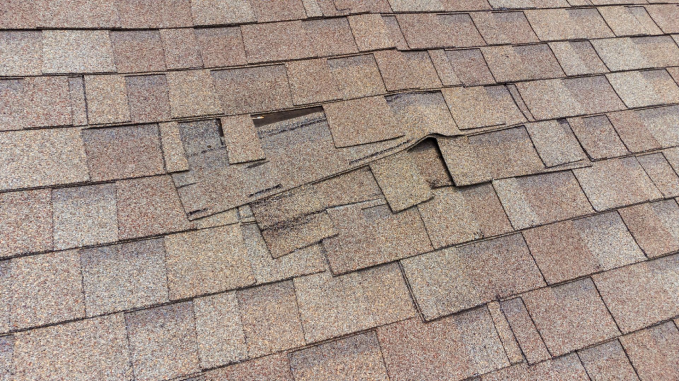 Damaged asphalt roof shingles with missing and broken pieces showing wear