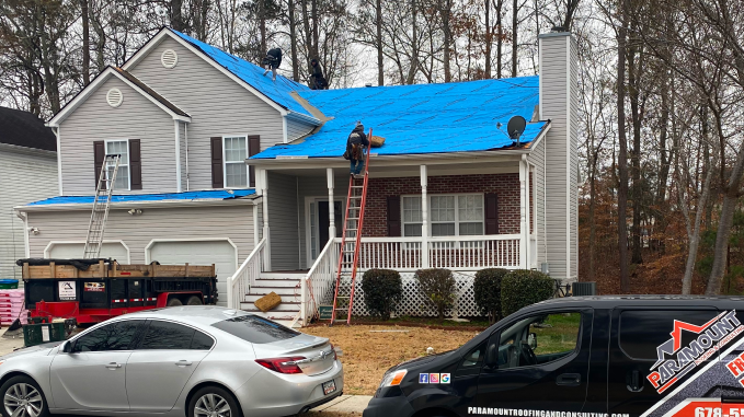 Roofers installing blue tarps on residential house roof after storm damage
