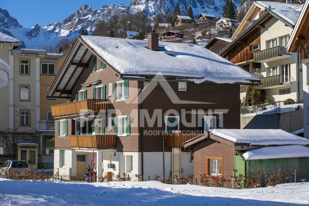 Snow-Covered Alpine Village Houses With Traditional Architecture Nestled Beneath Dramatic Mountain Peaks In Winter
