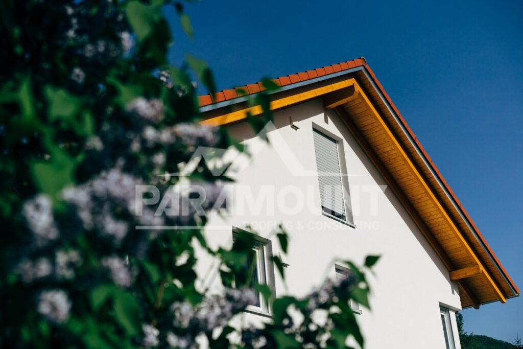 Modern White House With Orange Clay Tile Roof And Wooden Eaves Against Blue Sky, Framed By Blooming Tree