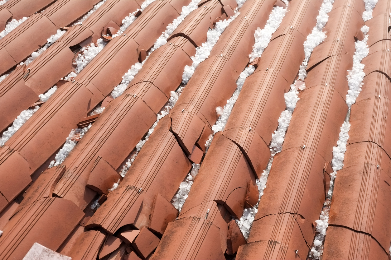 Damaged terracotta roof tiles with scattered hailstones.